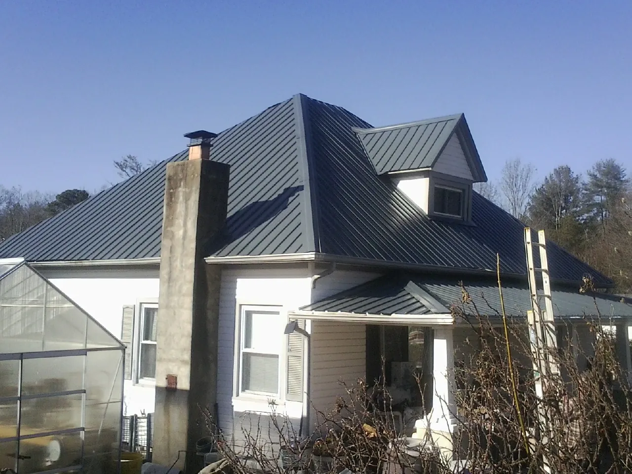 Dark blue standing seam metal roof on a white farmhouse with dormer — Slate & Tile Roof Repair by Roofing Brothers in Mendota