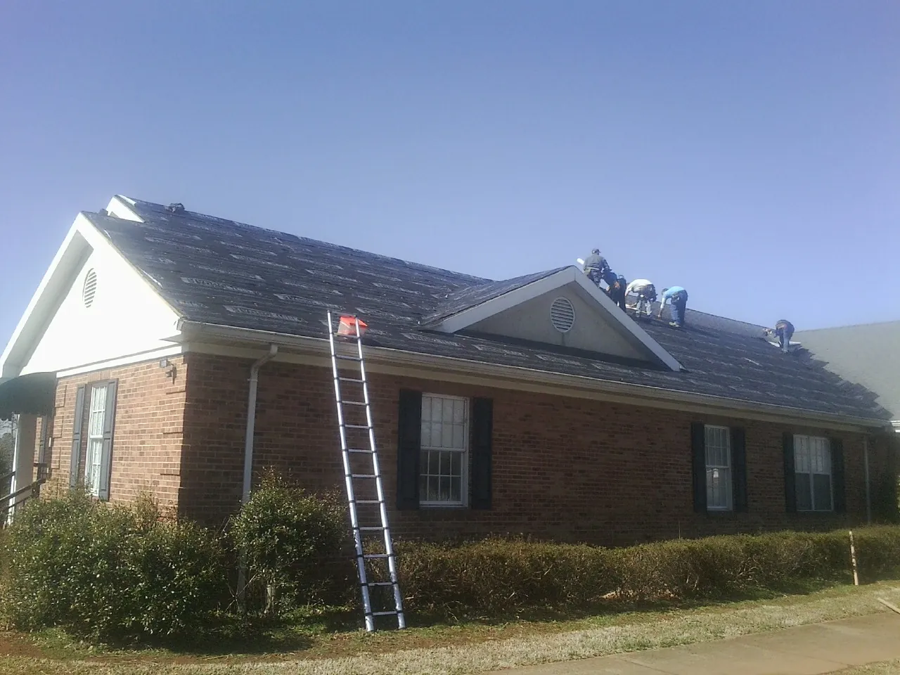 Crew tearing shingles off a brick ranch roof with a ladder set — Emergency Roof Repair work by our crew in Mendota