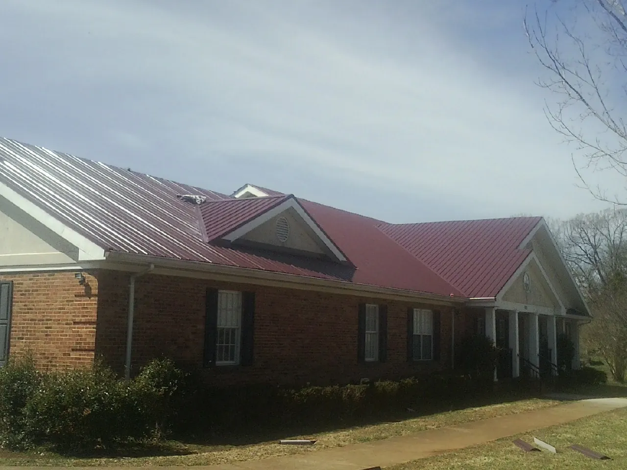 Red metal roof with gabled entries on a long brick building, from a Hail Damage Roof Repair job in Mendota