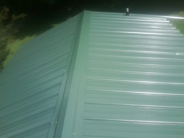 New green metal panels meeting at the ridge of a roof — Flat Roof Repair work by our crew in Mendota