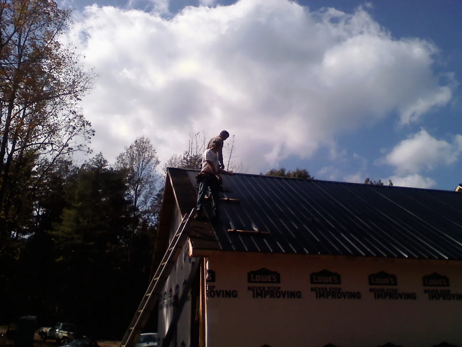 Roofer fastening dark metal panels high against a cloudy sky, from a Roof Inspection job in Mendota
